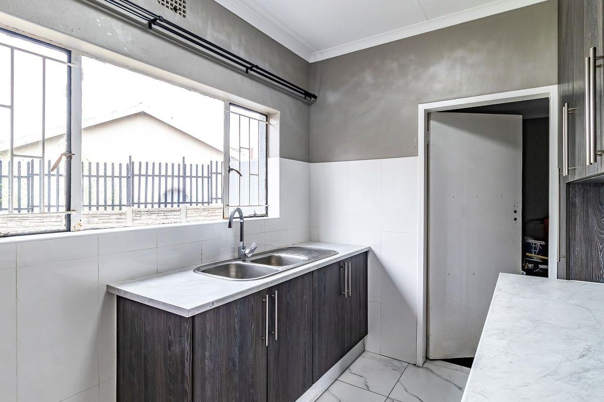 A functional kitchen area featuring dark wood cabinetry, marble-look countertops, a double stainless steel sink, and tiled flooring.