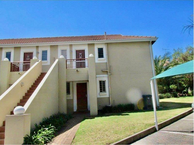 Exterior view of a two-story apartment building featuring a tiled roof, external staircase, and ground-level entrance with surrounding garden area.