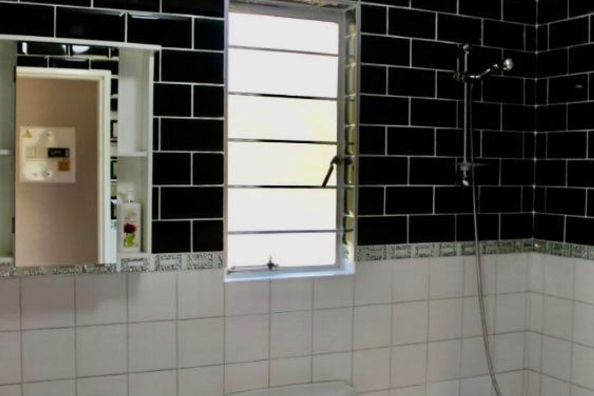 A functional bathroom featuring a pedestal sink, a standard toilet, and a shower-over-bath combination with contrasting black and white subway tiling.