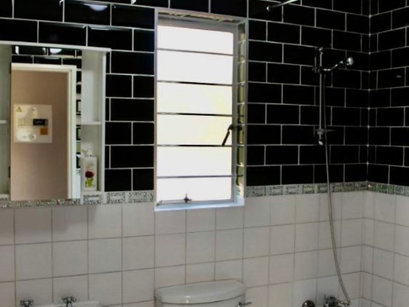 A functional bathroom featuring a pedestal sink, a standard toilet, and a shower-over-bath combination with contrasting black and white subway tiling.