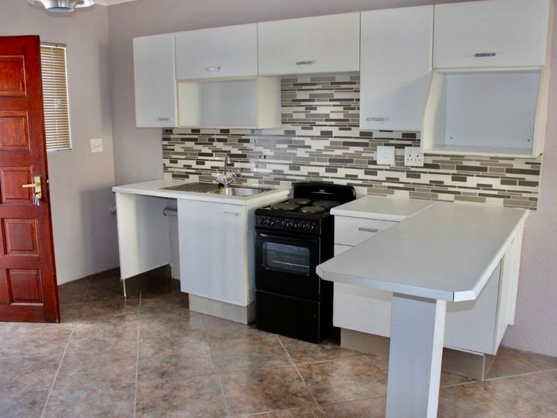 Compact kitchen featuring white cabinetry, a tiled backsplash, a built-in sink, and a freestanding electric stove with oven.