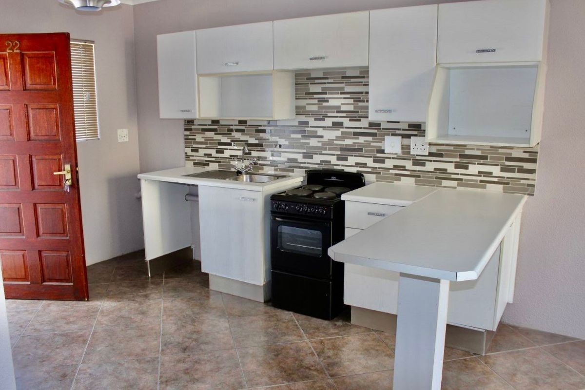 Compact kitchen featuring white cabinetry, a tiled backsplash, a built-in sink, and a freestanding electric stove with oven.