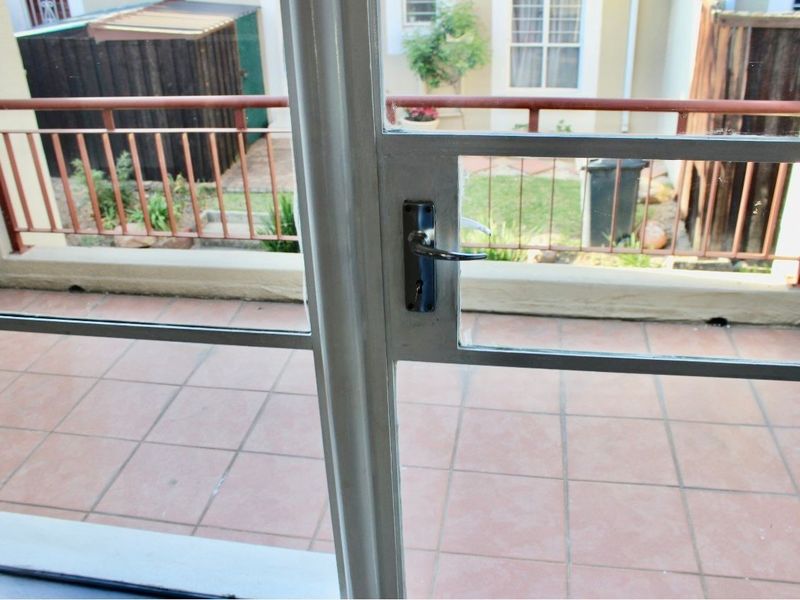 A view through a glass door onto a tiled balcony with metal railings, overlooking a small rear garden area.