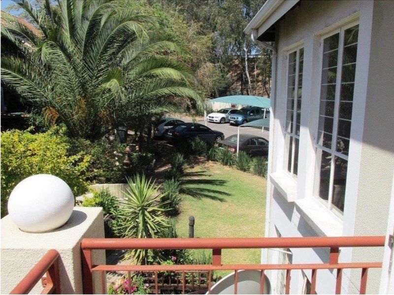 View from an apartment balcony overlooking a landscaped garden area with mature palm trees and a parking lot in the background.