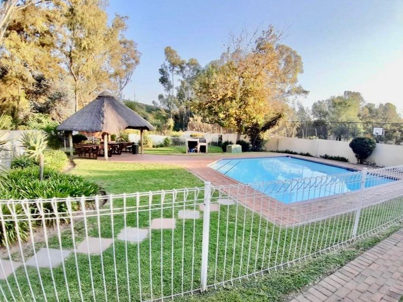 Outdoor pool area featuring a swimming pool, a thatched lapa, and a paved patio area set within a landscaped garden.