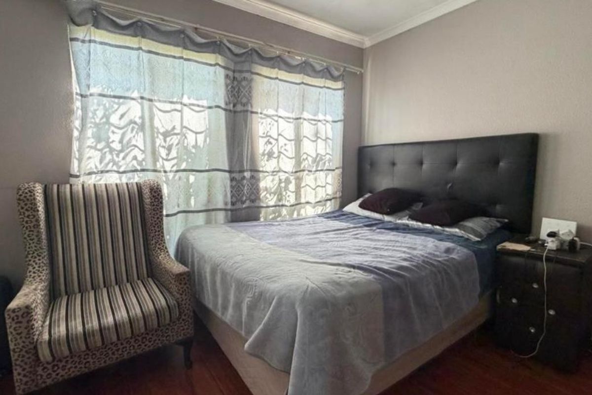 A bedroom featuring wooden flooring, neutral wall tones, and a large window with curtains, providing a comfortable and functional sleeping space.