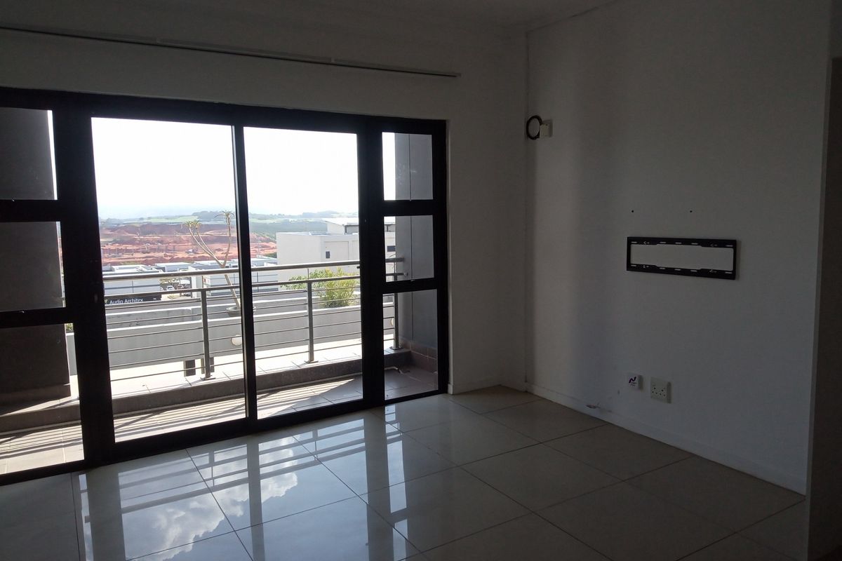 An empty living room featuring large sliding glass doors that open onto a balcony, with tiled flooring and neutral wall finishes.