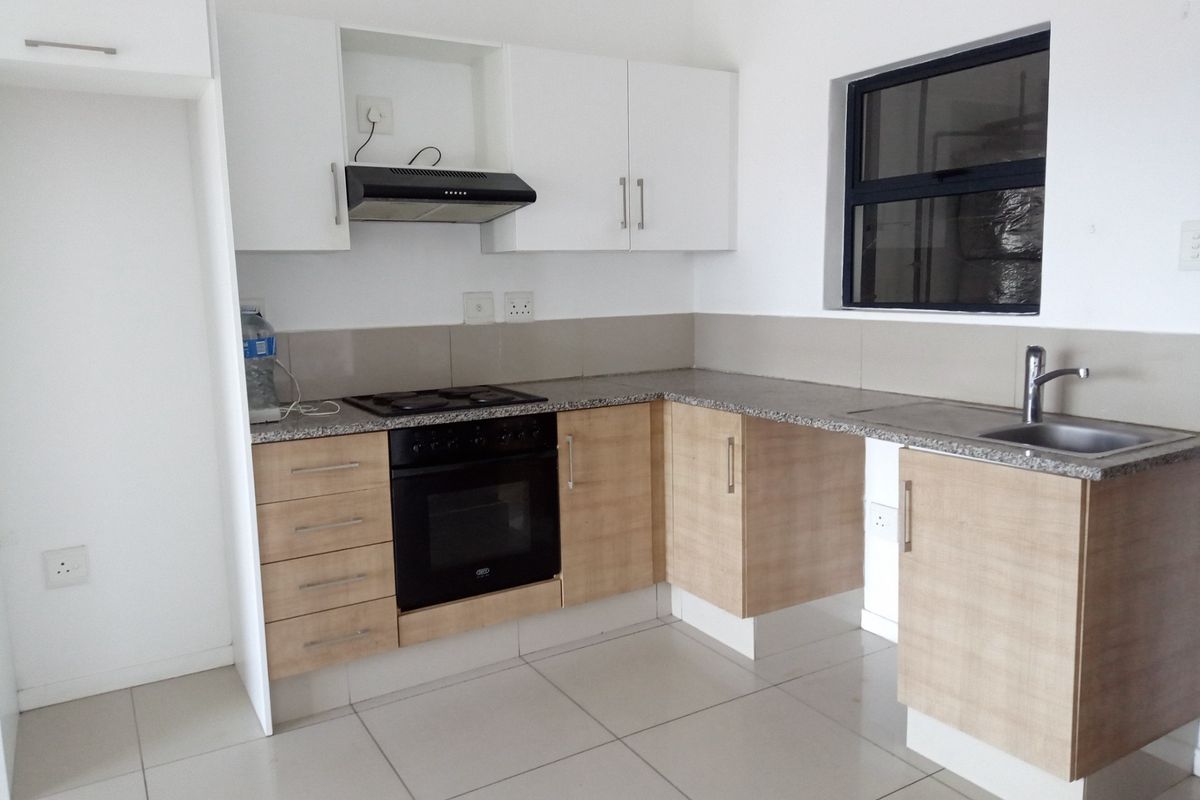 A functional kitchen featuring light wood-finish cabinetry, granite-look countertops, a built-in oven with hob, extractor fan, and a stainless steel sink.