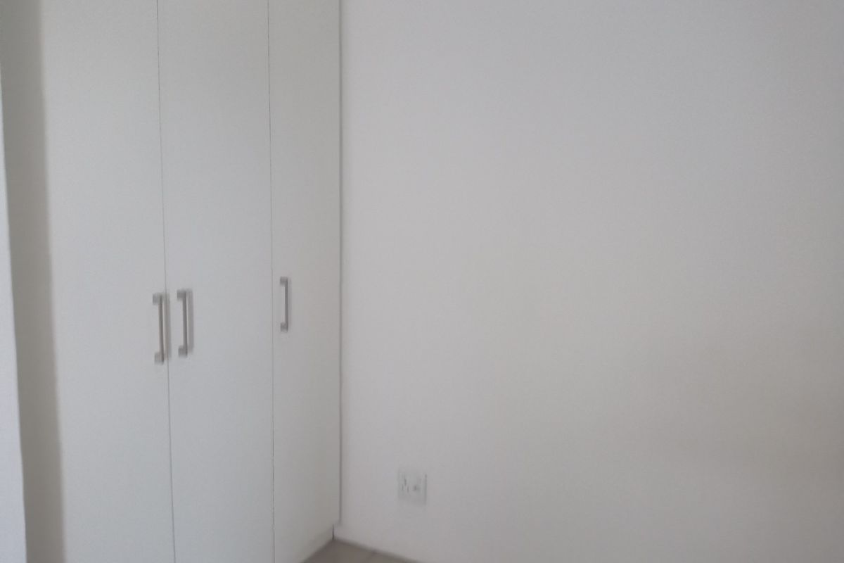 A bedroom interior featuring built-in white cabinetry with modern handles and neutral flooring.