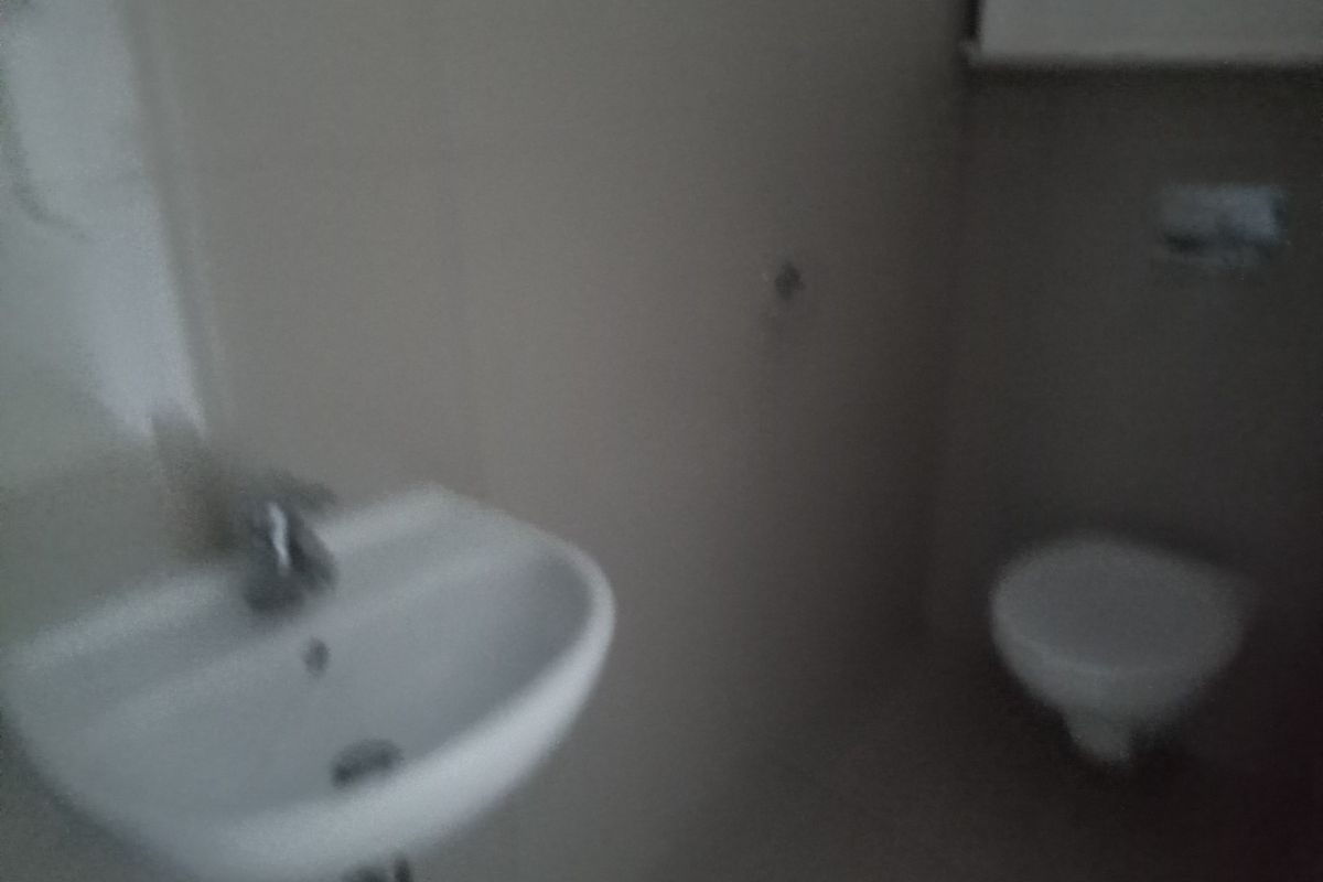 A small bathroom featuring a wall-mounted basin and a toilet, currently in need of better lighting and maintenance.