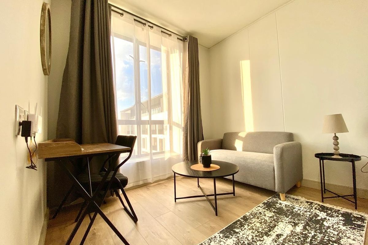 A bright living room featuring wood-look flooring, large windows with floor-to-ceiling curtains, and neutral wall finishes.