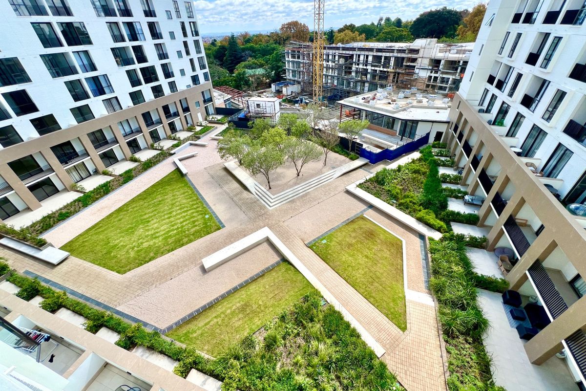 An elevated aerial view of a modern residential complex courtyard featuring landscaped lawns, paved walkways, and surrounding multi-story apartment buildings.