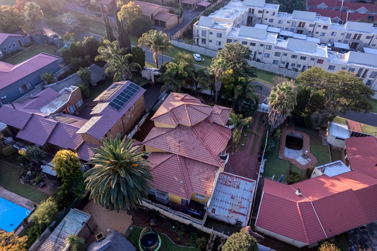 Aerial view of a residential property featuring a tiled roof, solar panels, and surrounding garden space within a suburban estate.