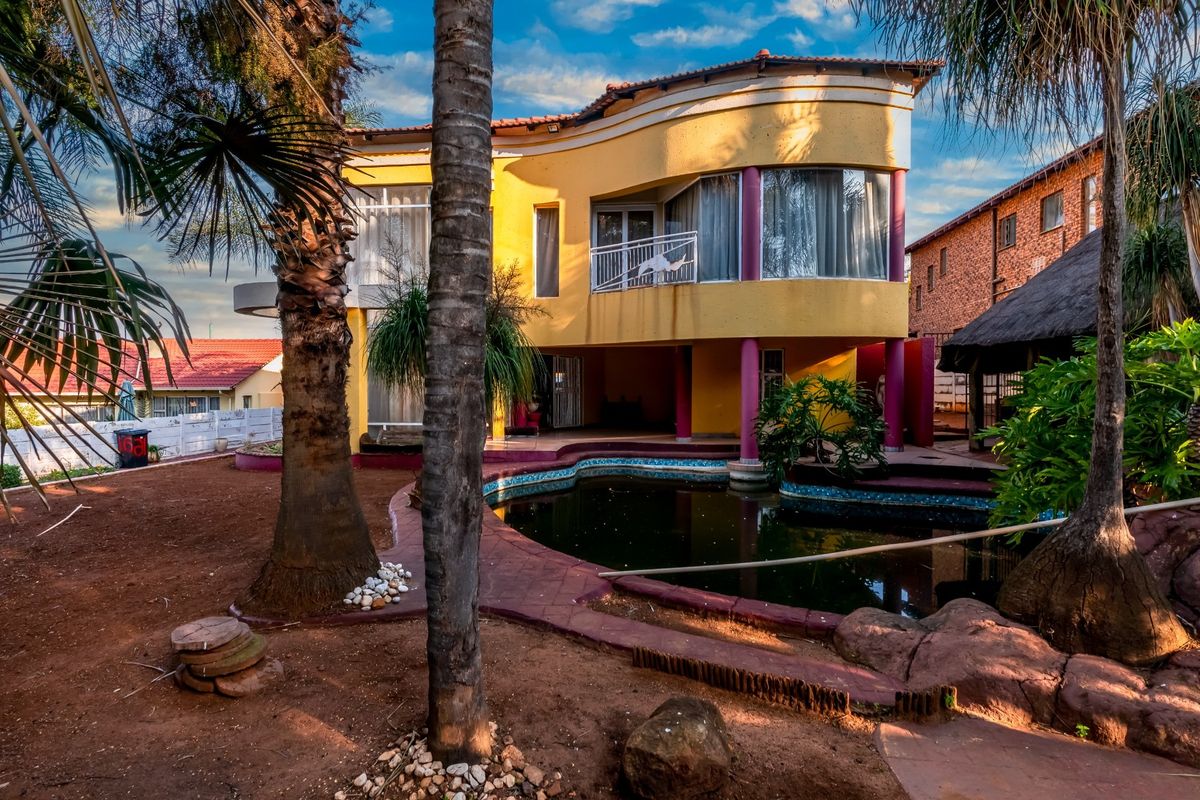 Rear view of a two-story house featuring a curved facade, balcony, and a swimming pool set within a large garden area.