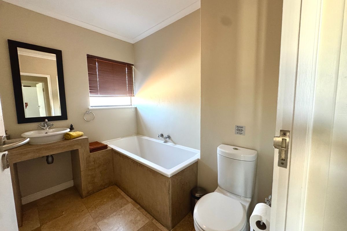 A functional bathroom featuring a built-in vanity with a vessel sink, a bathtub, and a standard toilet with tiled flooring.