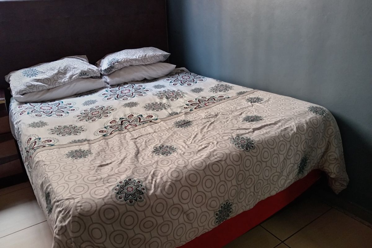 A bedroom featuring tiled flooring and a dark accent wall, providing a functional and neutral space for rest.