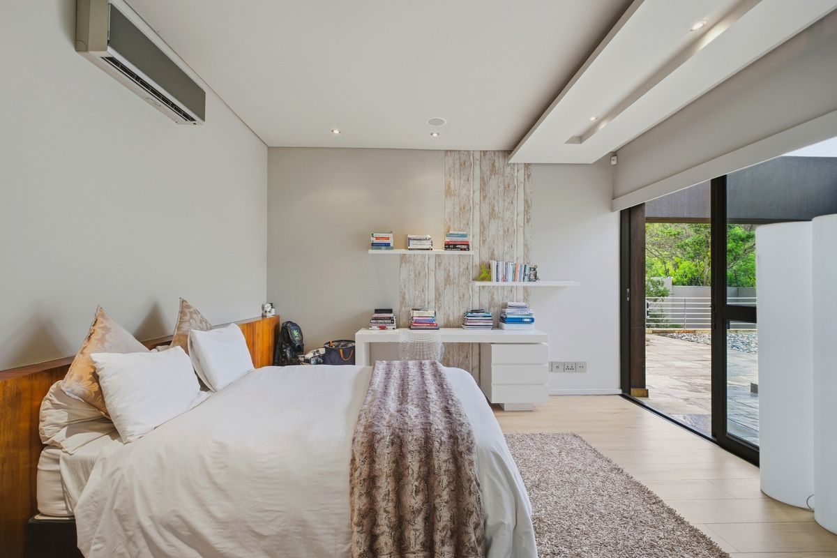 Modern bedroom featuring built-in desk, floating shelving, recessed ceiling lighting, wall-mounted air conditioning unit, and large sliding glass doors opening to a patio.