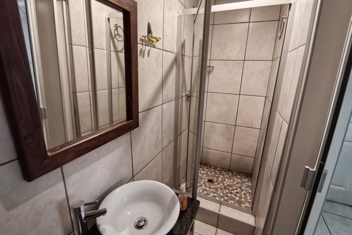 A compact bathroom featuring a modern vessel sink, granite vanity top, and a tiled shower enclosure with a pebble-style floor finish.