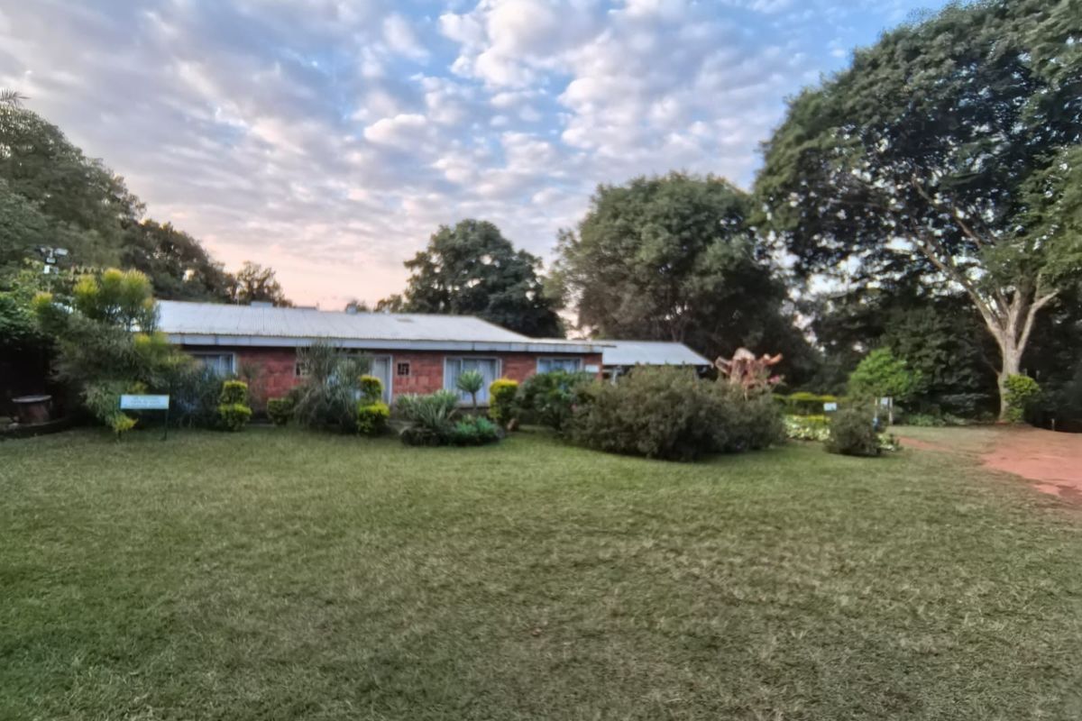A view of the property's exterior facade featuring a brick structure set within a spacious, well-established garden with mature trees.