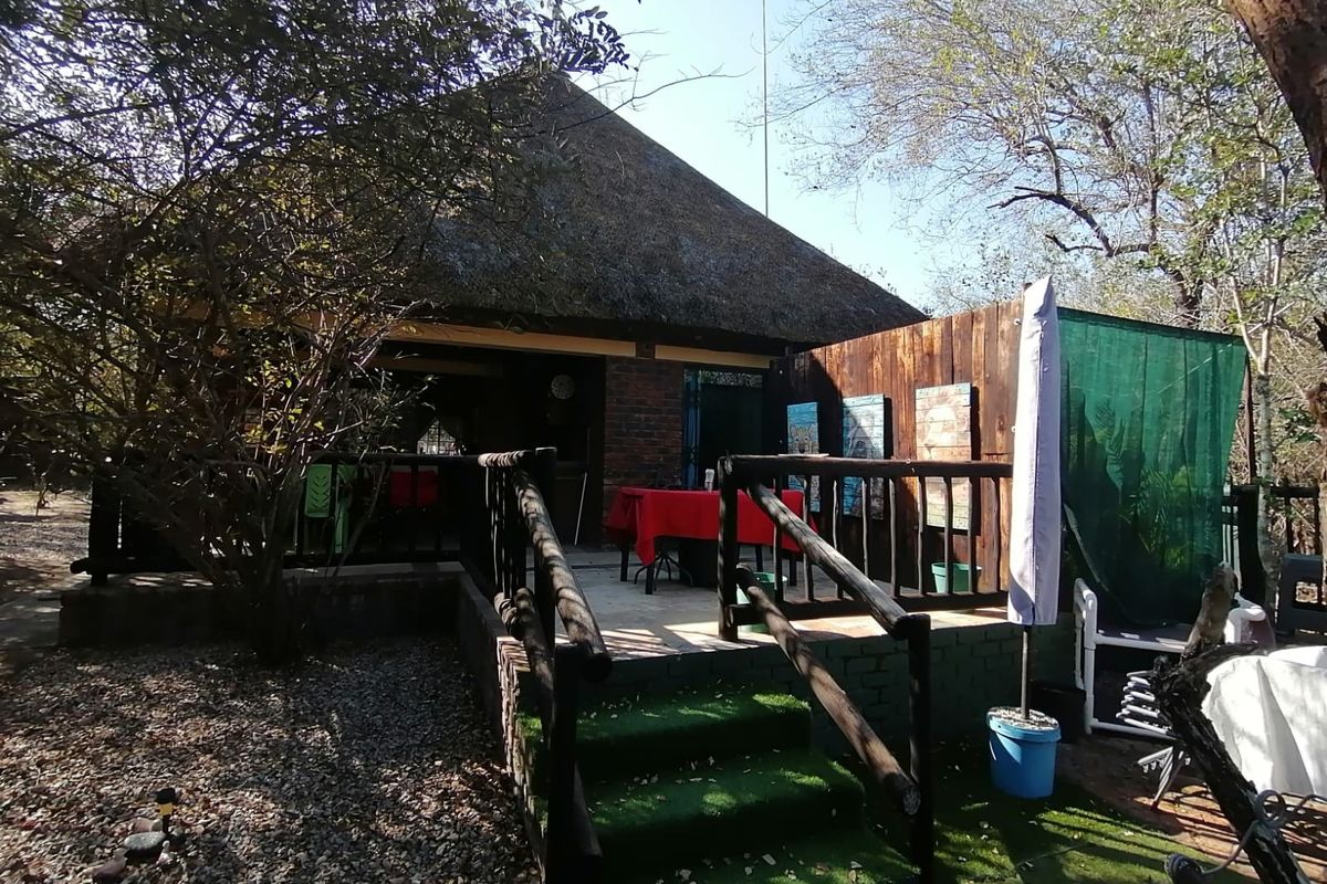 Rear view of a rustic house featuring a thatched roof, elevated timber deck, and brick exterior walls set within a natural garden environment.