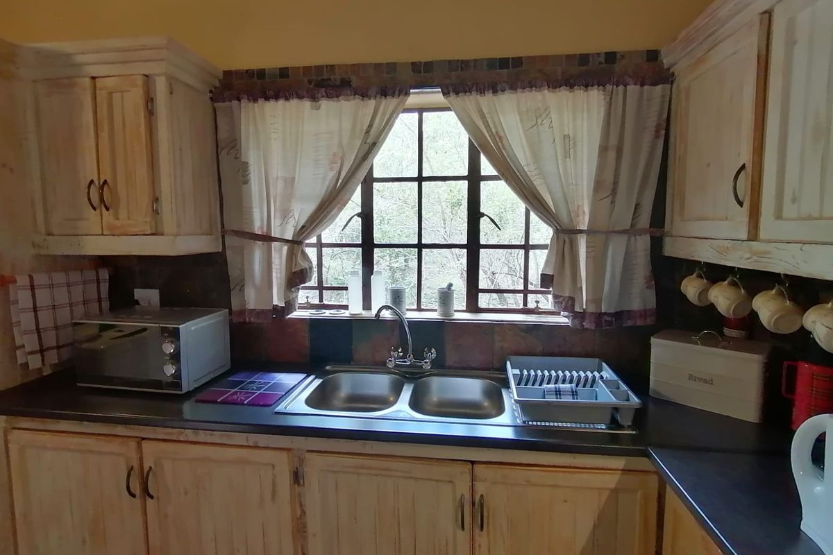 A functional kitchen featuring timber cabinetry, a double basin sink with a mixer tap, and a tiled splashback under a lattice window.