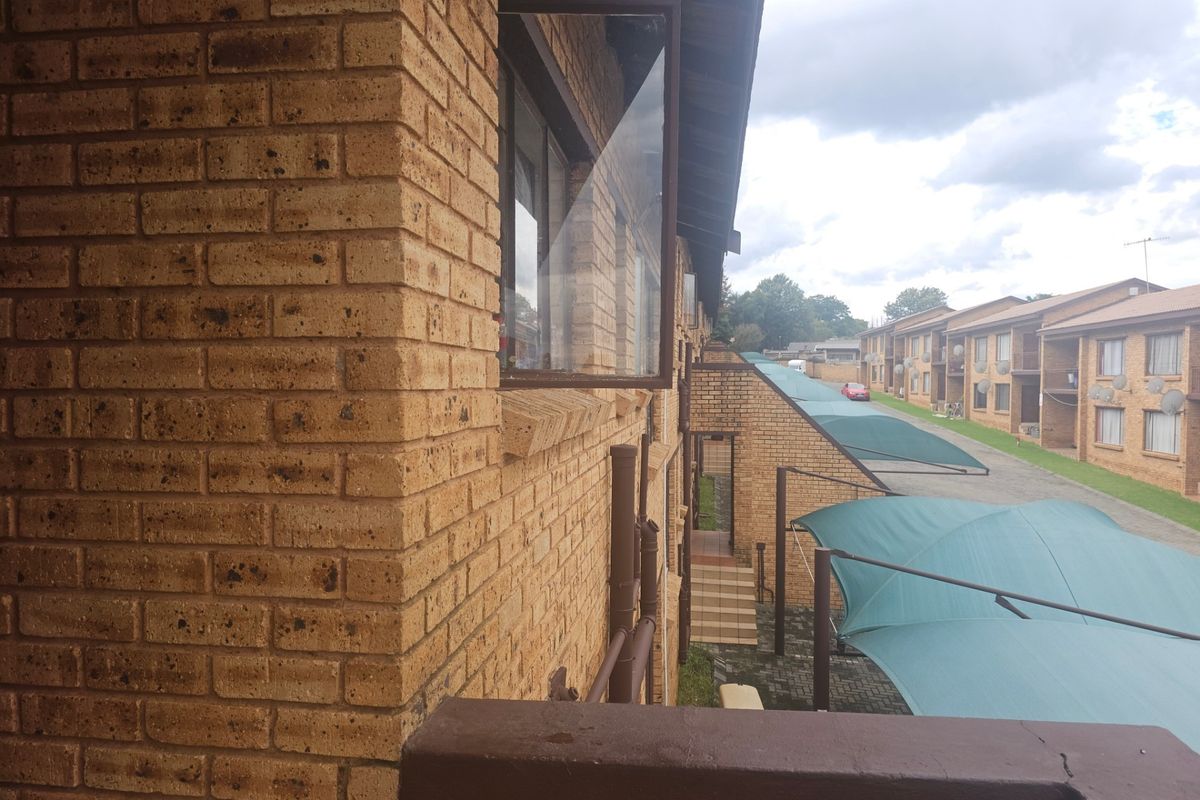 Exterior view of the apartment complex featuring face-brick facade, open window, and covered parking bays with shade cloth structures.