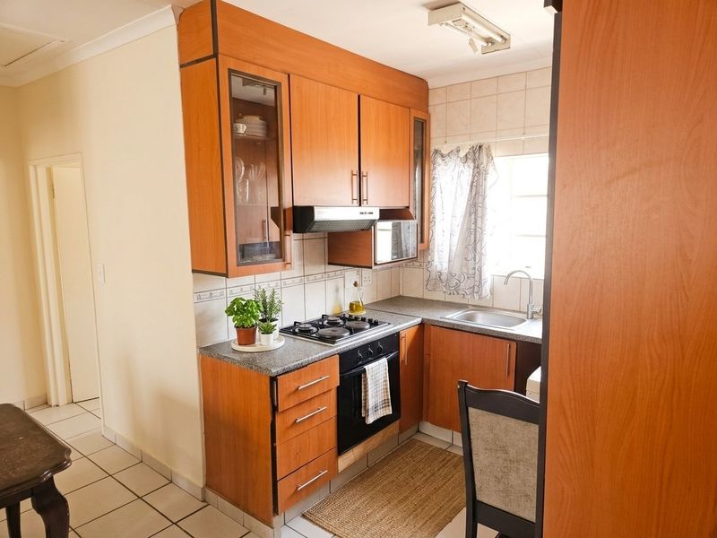 A functional kitchen featuring wooden cabinetry, a gas hob, built-in oven, extractor fan, and a stainless steel sink with tiled backsplash.