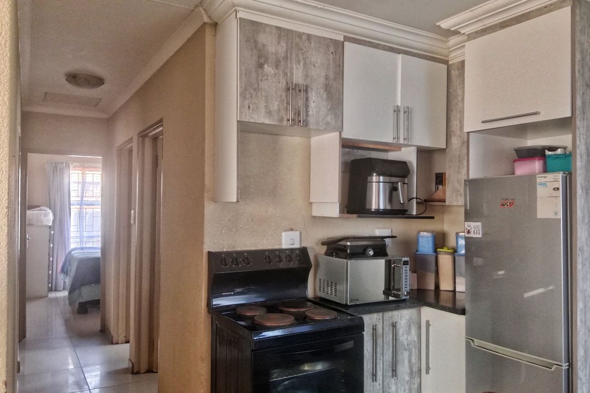 A functional kitchen area featuring built-in cabinetry, a freestanding stove, and tiled flooring, with a view leading into the hallway and bedroom.