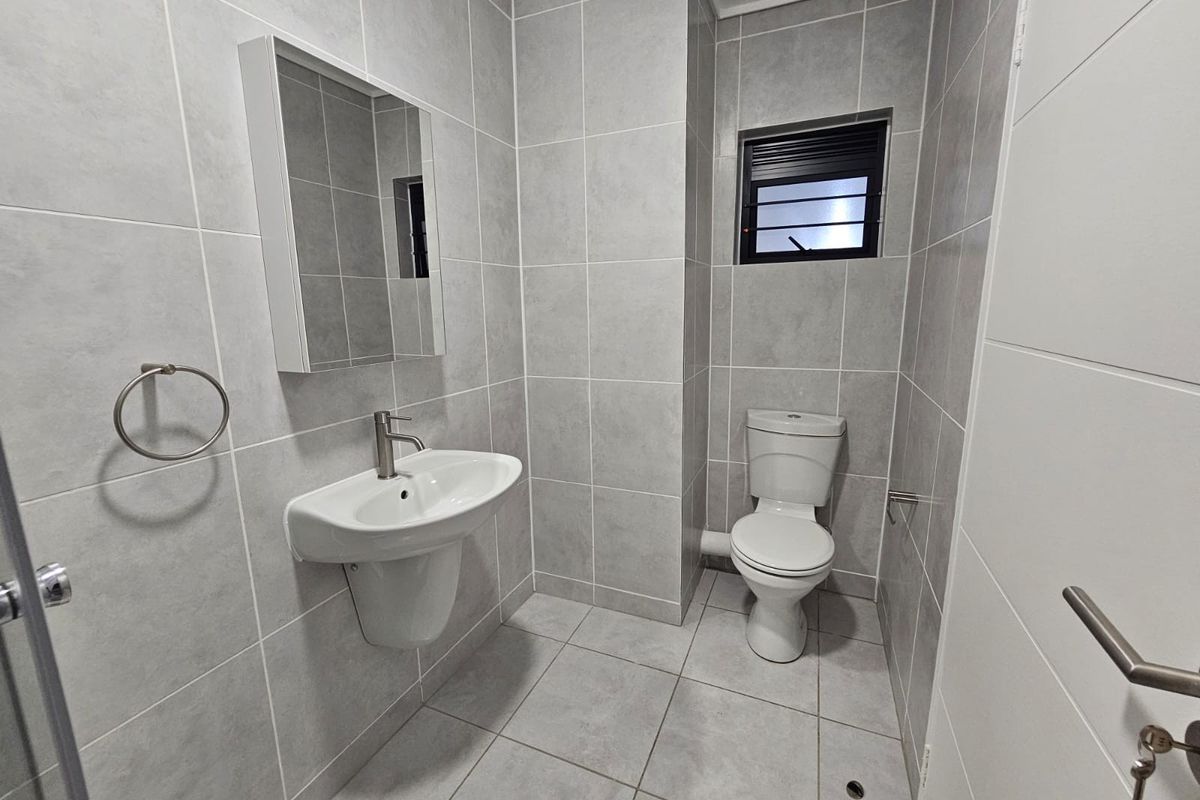 A modern, well-maintained bathroom featuring grey floor-to-ceiling tiling, a wall-mounted basin, a toilet, and a mirrored cabinet.