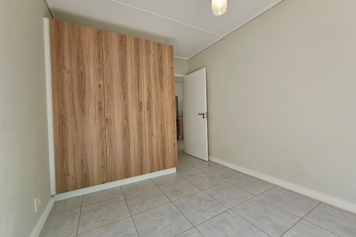 A clean, neutral bedroom featuring light grey floor tiles and built-in wood-grain cabinetry, offering a bright and functional living space.