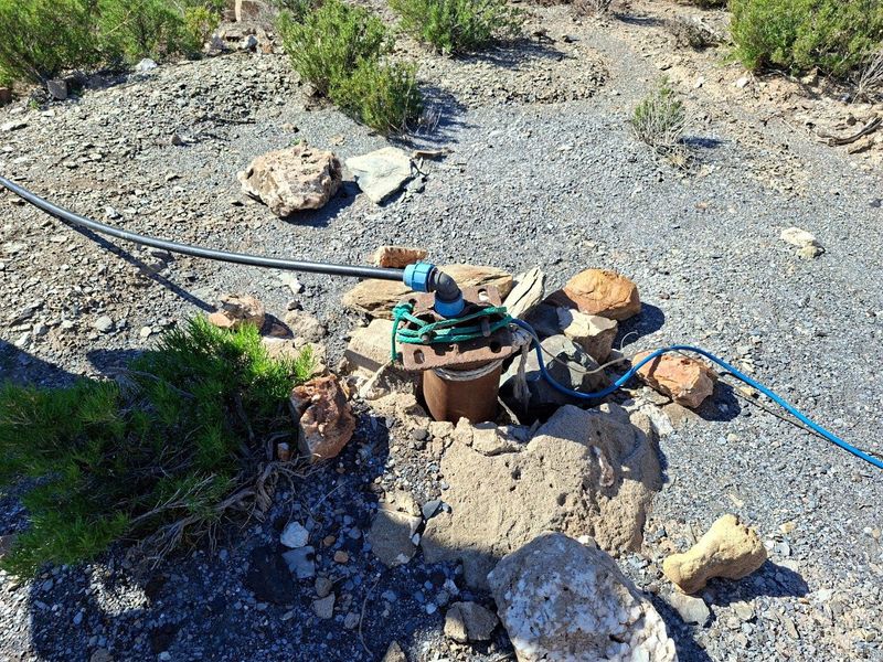 An exposed borehole installation on the property, featuring basic piping and electrical connections requiring maintenance and proper protective housing.