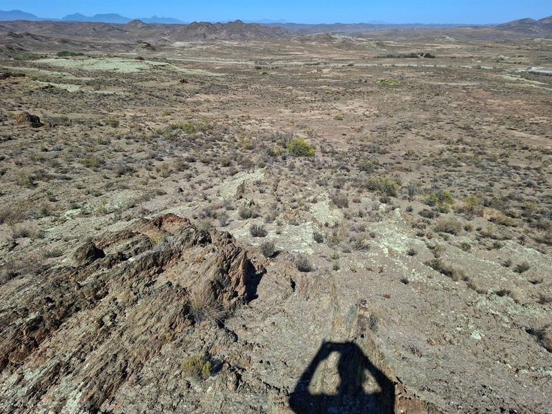 Expansive panoramic view of the rugged, arid farm landscape featuring rocky terrain and distant mountain ranges under a clear blue sky.