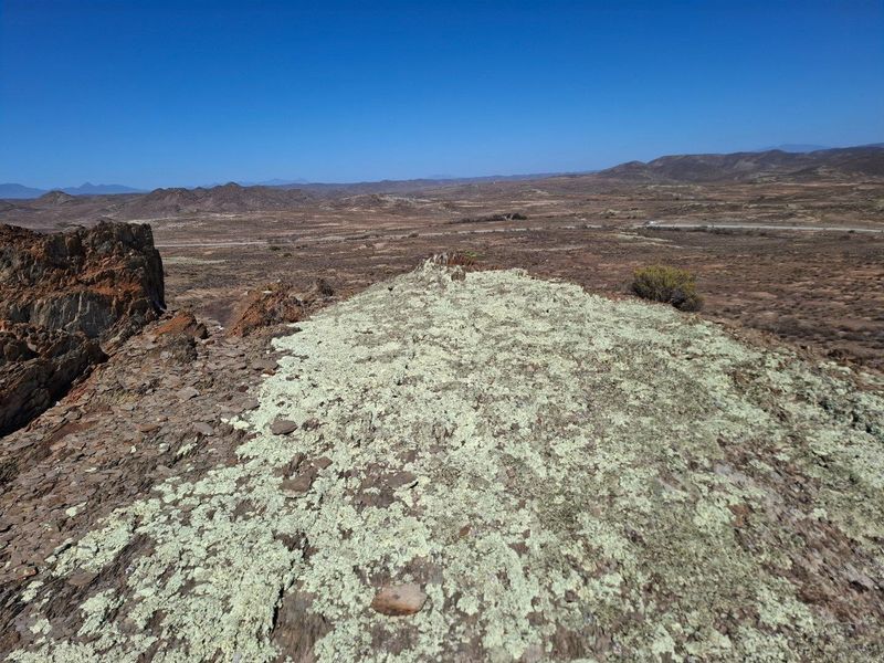 Expansive panoramic view of the surrounding arid landscape and mountain ranges from an elevated rocky vantage point.