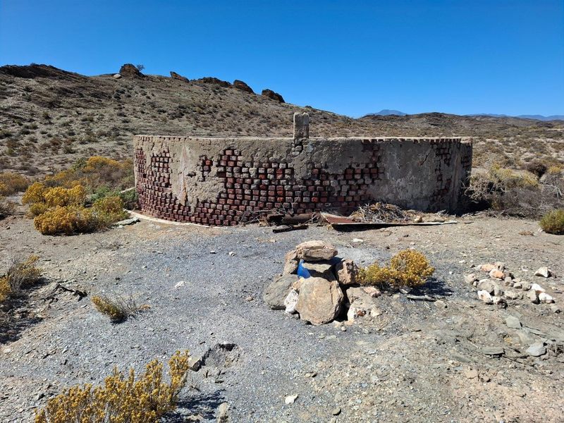 An old, weathered circular brick water reservoir situated in a rural landscape, showing significant signs of age and structural deterioration.