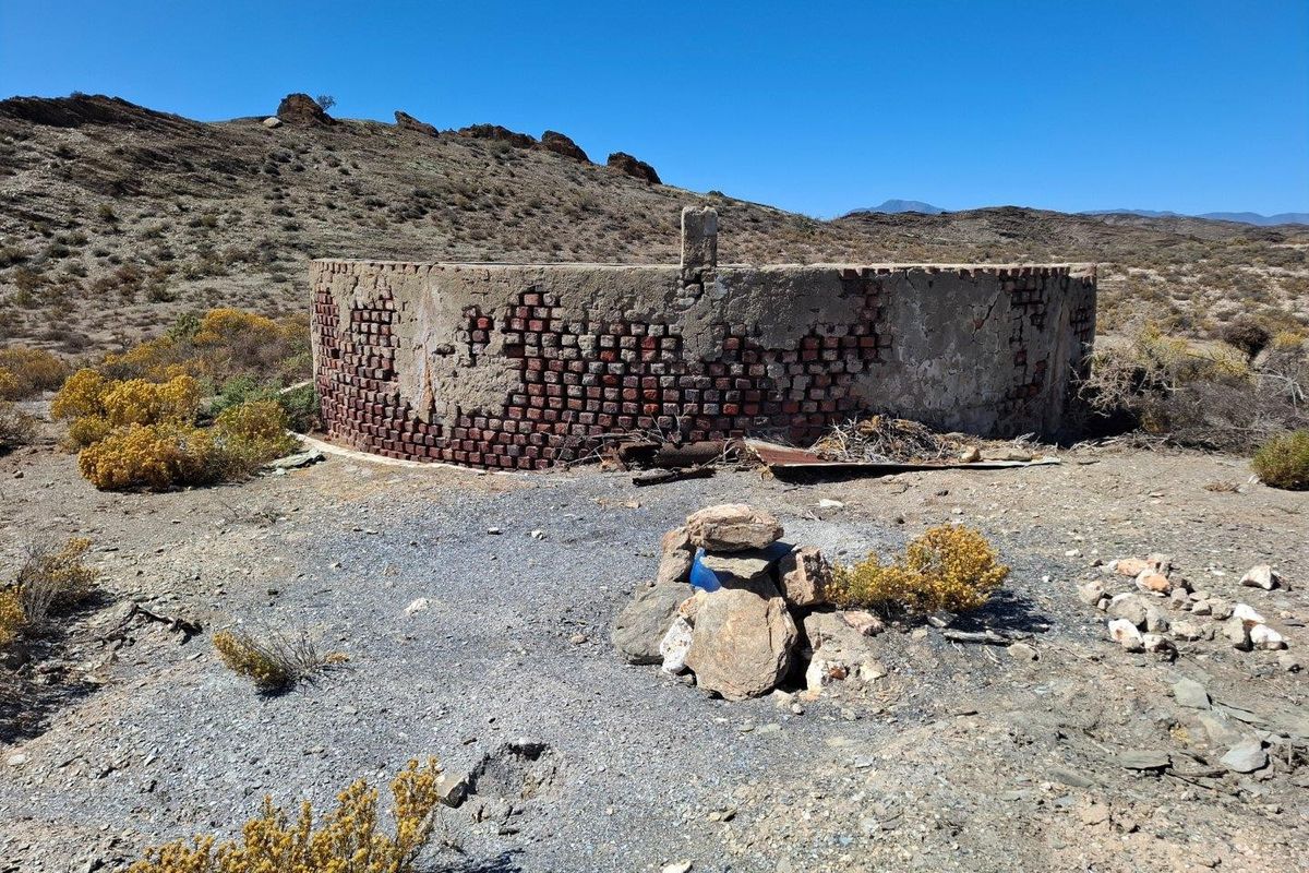 An old, weathered circular brick water reservoir situated in a rural landscape, showing significant signs of age and structural deterioration.