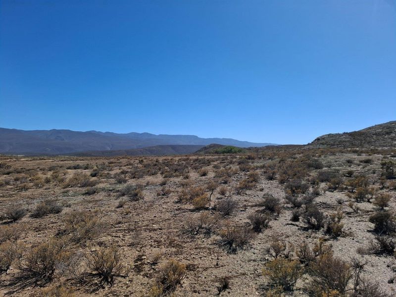 A wide-angle view of the expansive, arid landscape featuring natural scrub vegetation and distant mountain ranges under a clear blue sky.