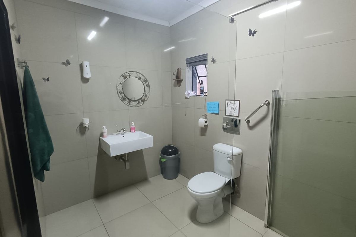 A functional bathroom featuring floor-to-ceiling wall tiles, a wall-mounted basin, a standard toilet, and a glass-enclosed shower area.