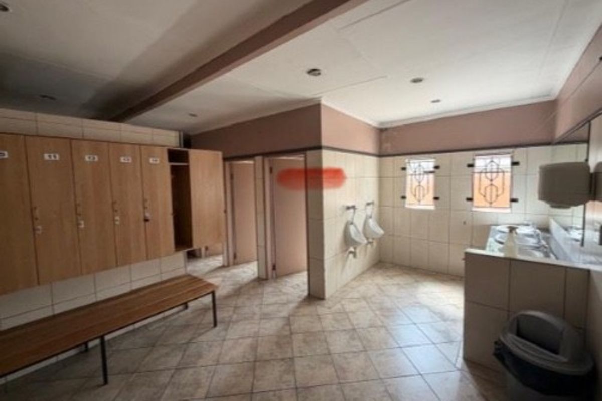 A functional commercial restroom facility featuring built-in wooden lockers, wall-mounted urinals, tiled flooring, and multiple partitioned cubicles.