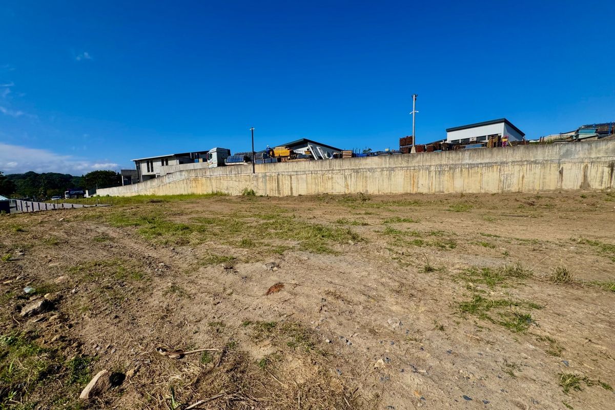 A view of the vacant agricultural land featuring a prominent concrete retaining wall along the boundary with neighboring structures visible in the background.