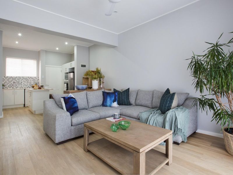 An open-plan living area featuring light wood-look flooring, recessed lighting, and a modern kitchen with a mosaic tile backsplash and island bench.