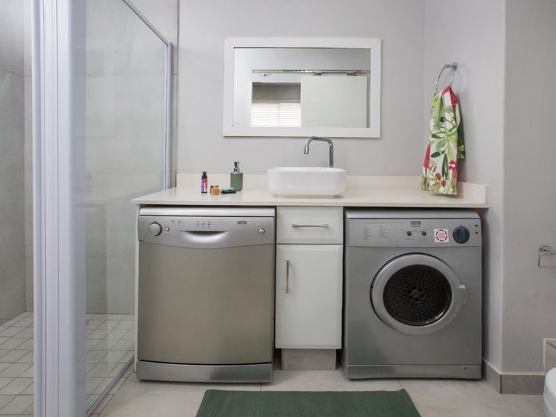 A functional laundry area featuring a built-in vanity with a countertop basin, integrated appliance spaces, and an adjacent glass-enclosed shower.