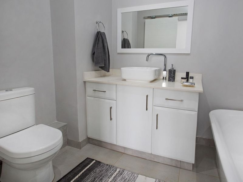 A modern bathroom featuring a white vanity with a vessel sink, a toilet, and a bathtub, finished with neutral wall tones and tiled flooring.