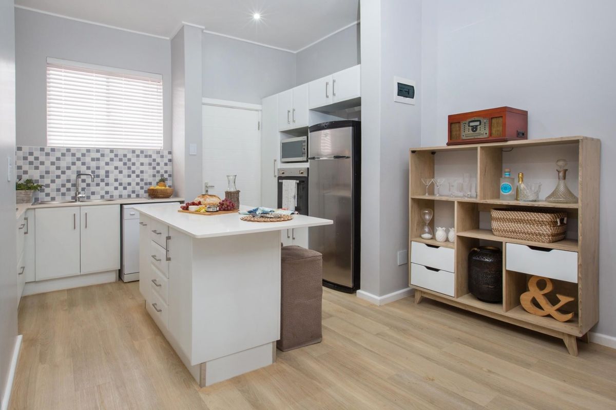 Modern kitchen featuring a central island, white cabinetry, mosaic tile backsplash, stainless steel appliances, and light wood-look laminate flooring.