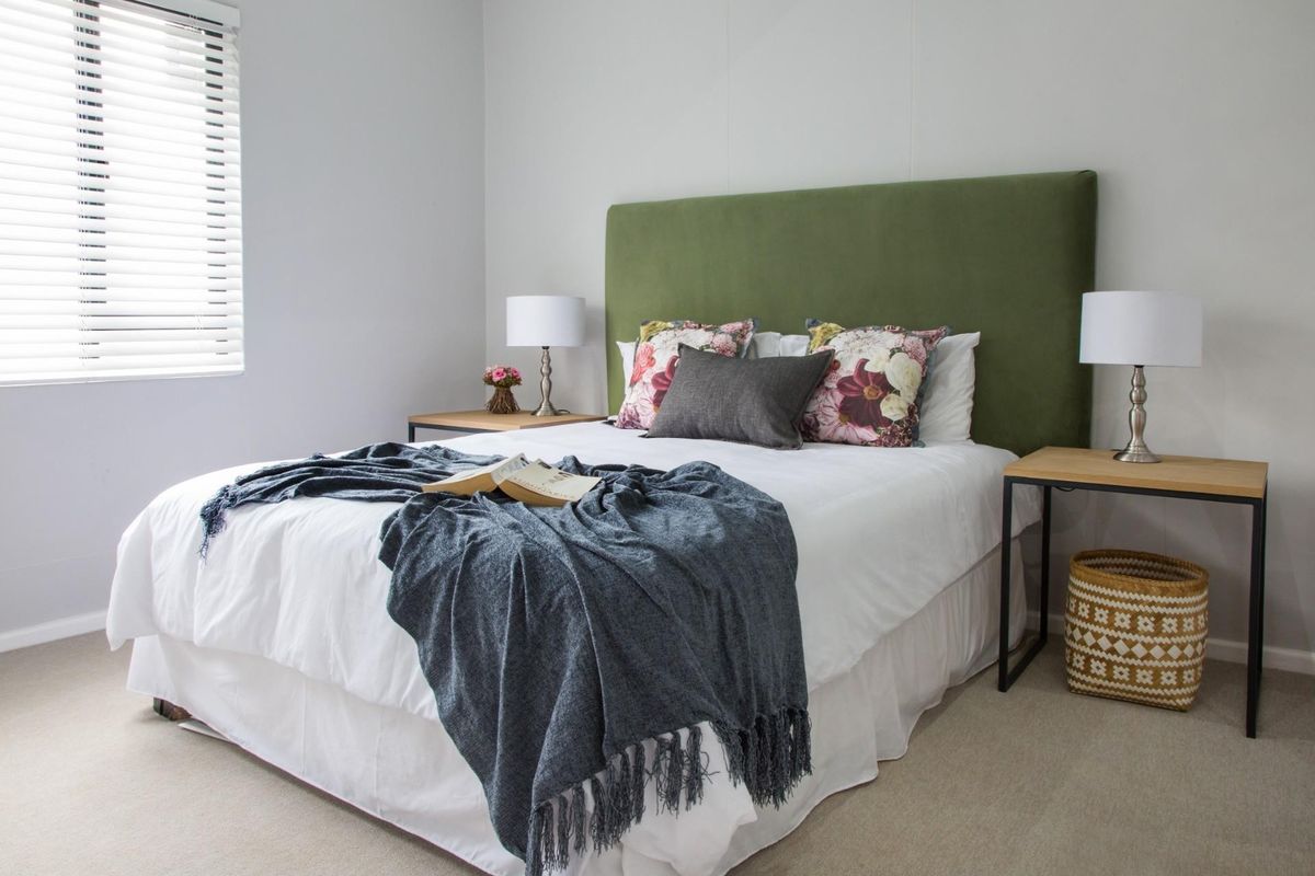 A well-maintained bedroom featuring neutral carpeted flooring and venetian blinds, providing a clean and comfortable living space.