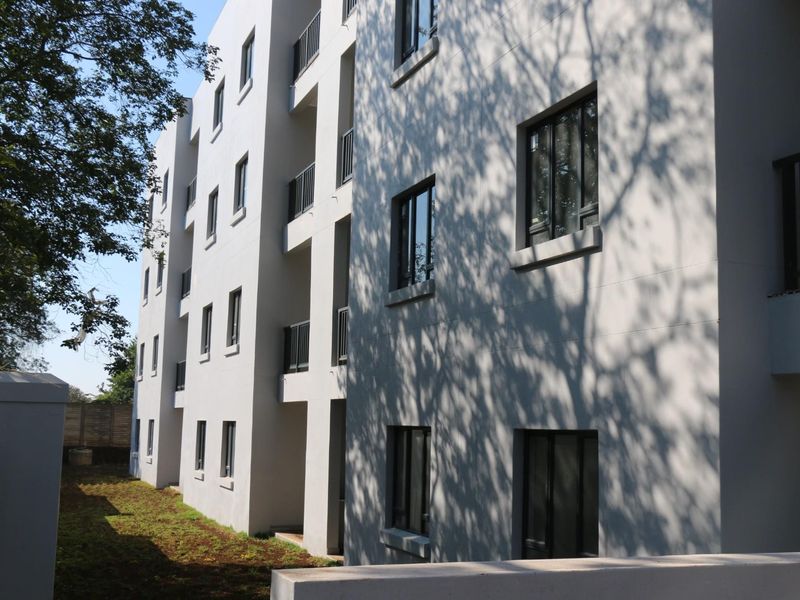 A view of the apartment building's rear facade, featuring modern painted exterior walls, aluminium window frames, and private balconies overlooking a garden area.