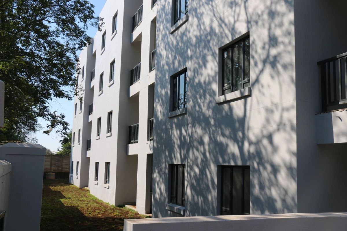 A view of the apartment building's rear facade, featuring modern painted exterior walls, aluminium window frames, and private balconies overlooking a garden area.