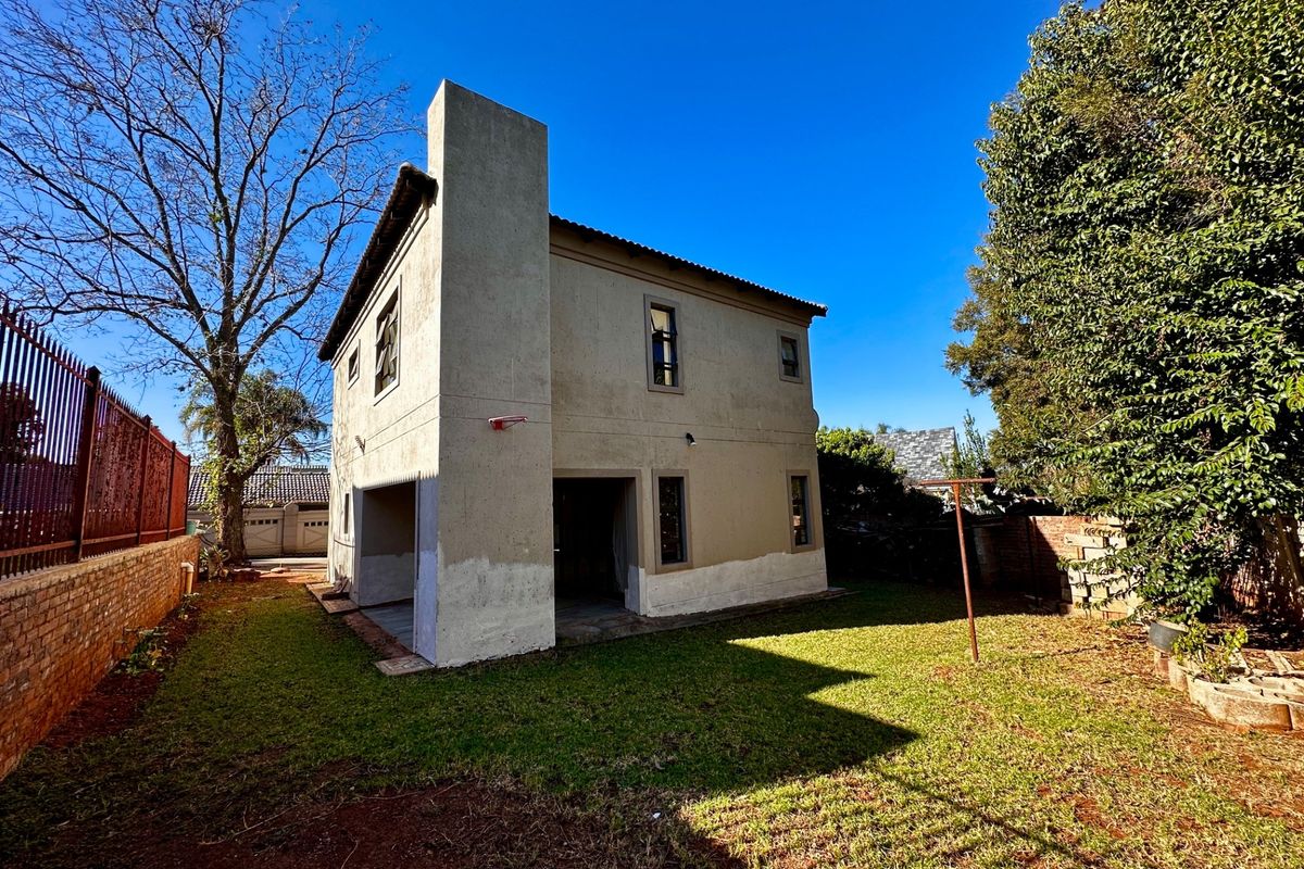 Rear view of a two-story residential house featuring a prominent chimney stack, covered patio area, and a private garden space.