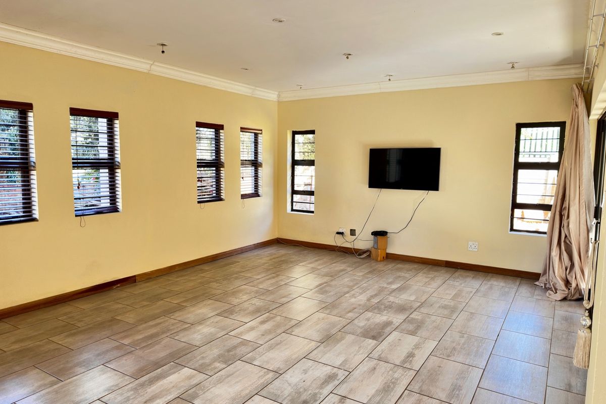 Spacious living area featuring neutral walls, tiled flooring, and multiple windows with fitted blinds, providing a bright and open atmosphere.