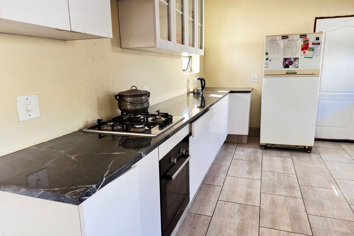 A functional kitchen featuring dark stone countertops, white cabinetry, a built-in oven, and a gas hob, complemented by tiled flooring.