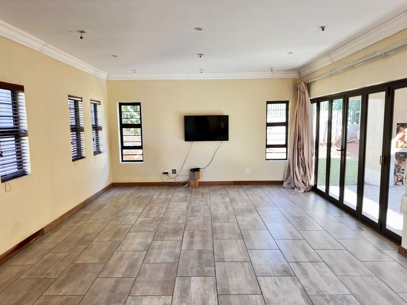 Spacious living room featuring wood-look ceramic floor tiles, recessed ceiling lighting, and large folding glass doors providing direct access to the outdoor area.